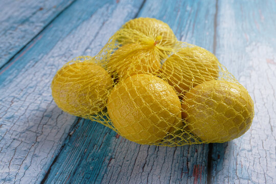 Close up of yellow lemons in a net package, on blue background.
