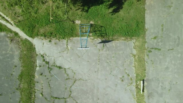 Old basketball backboard. Made from boards. Peeling paint and a battered basket. There is an old cracked asphalt on the site. The camera descends vertically into a basketball hoop. Aerial photography