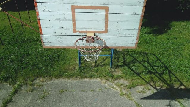 Old basketball backboard. Made from boards. Peeling paint and a battered basket. There is an old cracked asphalt on the site. The camera is fixed at the level of the shield. Aerial photography.