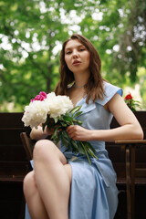 A beautiful young woman in a blue dress with a bouquet of peonies.