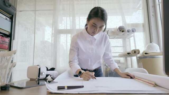 4K resolution Asian female architect or engineer designer working with blueprint planning on workplace. Architect woman working in office.