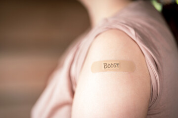 female with rolled up shirt sleeve to show the bandaid after the booster dose vaccine shot in the...