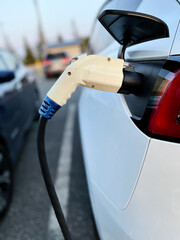 Electric vehicle being charged while parked. White charger is plugged into side of car.