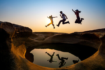 silhouette of group tourist people  jumping on a rock reflection on water,Vivid sunset sky.