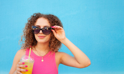 Beautiful happy woman with orange cold juice, concept summer drinks, rest and vacation. Blue background, isolated, copy space. Smiling, enjoying life, healthy and refreshing smoothie. sunglasses