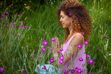 woman hands in namaste gesture outdor in summer field with flowers
