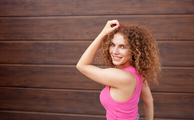 beautiful curly woman walks in city, against backdrop of brown wall, copy space for text. Happy, cheerful, smiling. pink top