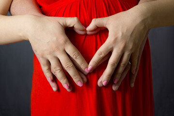 pregnant woman and her mate holding hands in a heart shape on belly
