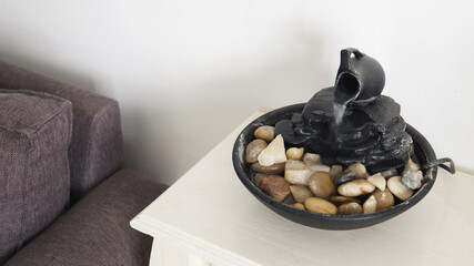 Top view of a decorative zen water fountain on top of a small white table. A white wall as a...