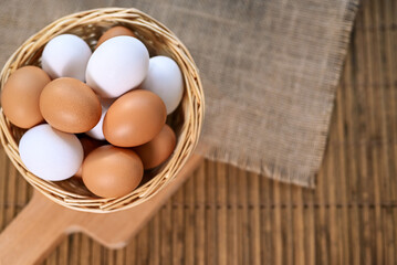 Background with chicken eggs. White and brown organic raw eggs in a basket on a bamboo mat.