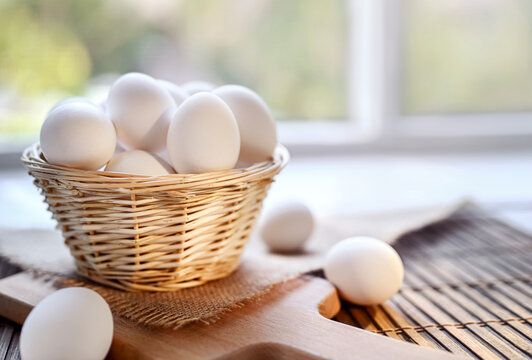 Raw organic white chicken eggs in a wicker basket on the table. Daylight, window, space for text.