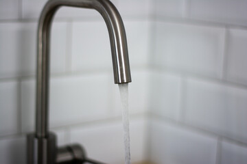 thin stream of water flowing from the tap against a white tile in the kitchen