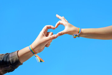 Close up of Woman hands in a rainbow bracelet making a heart shape form on blue sky background....