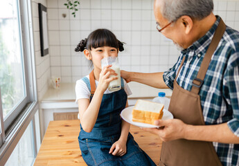 Asian granddaughter drinking milk with grandfather while sitting  in kitchen.Having Fun Together at Home. Happy Multi-Generation Family Enjoying Milk And  Laughing.