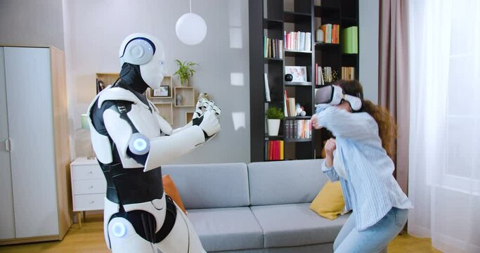 Robot fist bumping with attractive woman in VR goggles in living room. Concept of people, innovation and artificial intelligence.