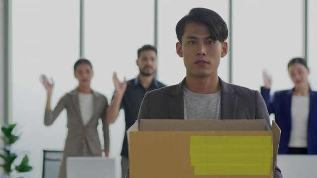 Portrait of jobless asian male emloyee fired from work. Upset young man with box full of things in hands looking at camera. Indoors. Firing from job. Crisis and business
