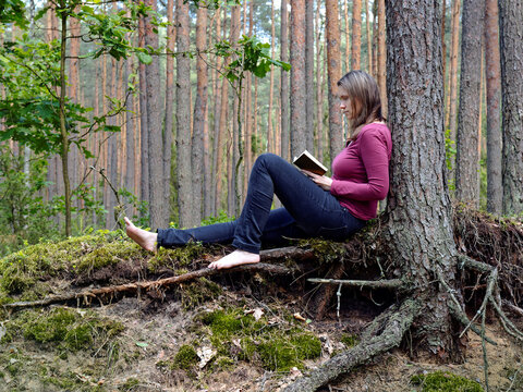 Person reading notebook sitting under the tree in the forest. Barefoot woman relaxing in nature.