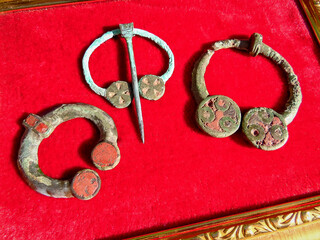 Antique bronze jewelry: brooches with enamels of the 3rd-5th centuries. AD Eastern Europe. Kyiv culture. On a red cloth in a frame
