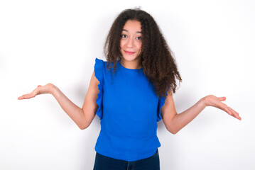 Clueless Teenager girl with afro hairstyle wearing blue T-shirt over white wall  shrugs shoulders...