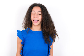 Teenager girl with afro hairstyle wearing blue T-shirt over white wall  sticking tongue out happy with funny expression. Emotion concept.