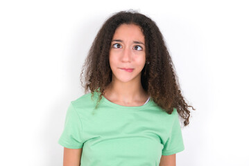 Teenager girl with afro hairstyle wearing green T-shirt over white wall making grimace and crazy face, screaming out of control, funny lunatic expressing freedom and wild.