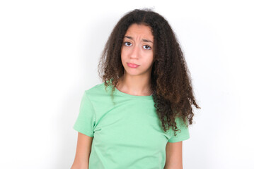 Displeased upset Teenager girl with afro hairstyle wearing green T-shirt over white  frowns face as going to cry, being discontent and unhappy as can't achieve goals,  Disappointed model has troubles