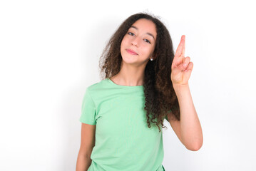 Teenager girl with afro hairstyle wearing green T-shirt over white wall pointing up with fingers number ten in Chinese sign language Shi