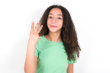 Teenager girl with afro hairstyle wearing green T-shirt over white wall smiling and looking...