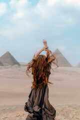 Back view of the young redhead girl with raised hands watching the Great Pyramids of Giza in Egypt