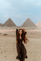 Young redhead tourist girl with raised hands in Egypt, Cairo - Giza. Pyramids on backround. Copy space