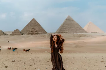 Foto op Canvas Young redhead tourist girl wearing a brown dress standing on the sand in Egypt, Cairo - Giza. Pyramids on backround. Copy space © Nikolay
