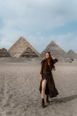 Young redhead tourist girl wearing a brown dress standing on the sand in Egypt, Cairo - Giza. Pyramids on backround. Copy space