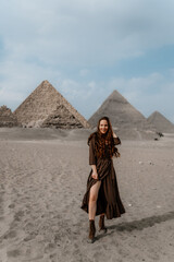 Young redhead tourist girl wearing a brown dress standing on the sand in Egypt, Cairo - Giza. Pyramids on backround. Copy space