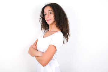 Portrait of Teenager girl with afro hairstyle wearing white T-shirt over white wall  standing with folded arms and smiling