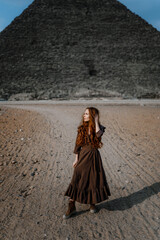 Young redhead tourist girl wearing a brown dress standing on the sand in Egypt, Cairo - Giza....