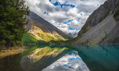 Picturesque mountain lake in the dramatic summer day, Altai. Beautiful reflection of mountains and white clouds. Panoramic view.