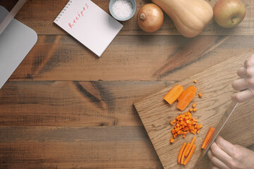A man cuts carrots on a wooden cutting board.