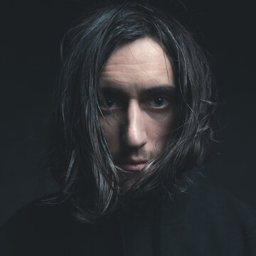 Cold portrait of a young man with a scary in view long hair on a black background