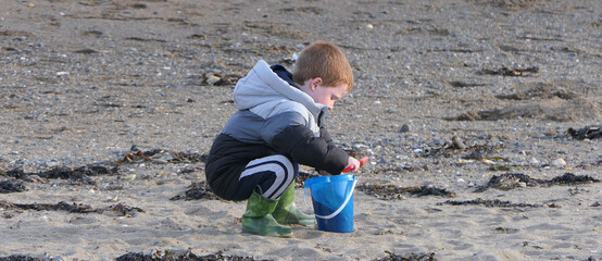 Red headed boy playing with Bucket spade and Digger on sandy beach