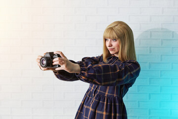 Girl teenager in dress holds retro camera in her hands, makes snapshot and smiles