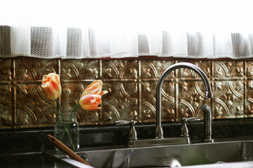 A small vase with fresh cut orange and yellow tulip flowers sitting on the back of a kitchen sink...