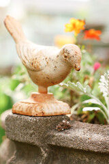 Garden decor bird statue sitting amongst flowers and a bird bath.