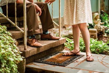 Feet and shoes of a male and female standing outside at the front steps of their home. 