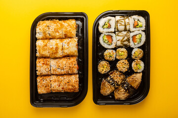 Delicious sushi rolls in disposable boxes on a yellow background. Food delivery concept. Food in the office. Japanese food. Flat lay top view, with copy space and space for text.
