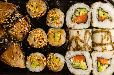 Delicious sushi rolls in disposable boxes on a yellow background. Food delivery concept. Food in the office. Japanese food. Flat lay top view, with copy space and space for text.