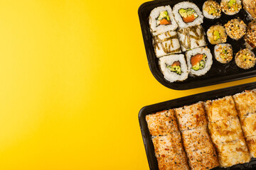 Delicious sushi rolls in disposable boxes on a yellow background. Food delivery concept. Food in the office. Japanese food. Flat lay top view, with copy space and space for text.