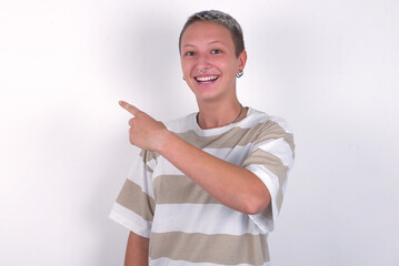 young woman with short hair wearing striped t-shirt over white background pointing away and smiling to you. Look over there!