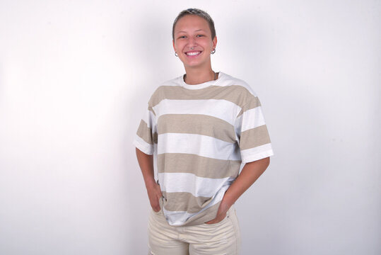 Portrait of successful young woman with short hair wearing striped t-shirt over white background, smiling broadly with self-assured expression. Confidence and business concept.