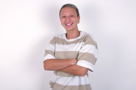 young woman with short hair wearing striped t-shirt over white background being happy smiling and crossed arms looking confident at the camera. Positive and confident person.