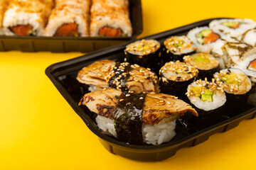 Delicious sushi rolls in disposable boxes on a yellow background. Food delivery concept. Food in the office. Japanese food. Flat lay top view, with copy space and space for text.
